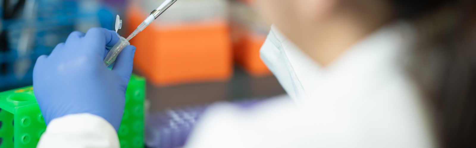 Lab technician wearing gloves uses pipette to transfer liquid into a tube in a blurred background of a lab