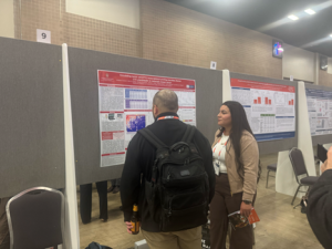 A man with a backpack, a San Antonio Breast Cancer Symposium attendee, discusses with Viridiana Carreno about her scientific research poster.